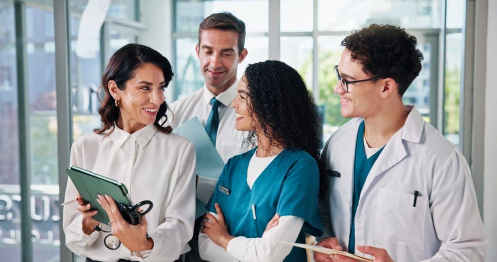 Happy people, doctor or meeting with tablet for medical research, discussion or development at hospital. Group, employees or healthcare workers with smile on technology for online app or telehealth