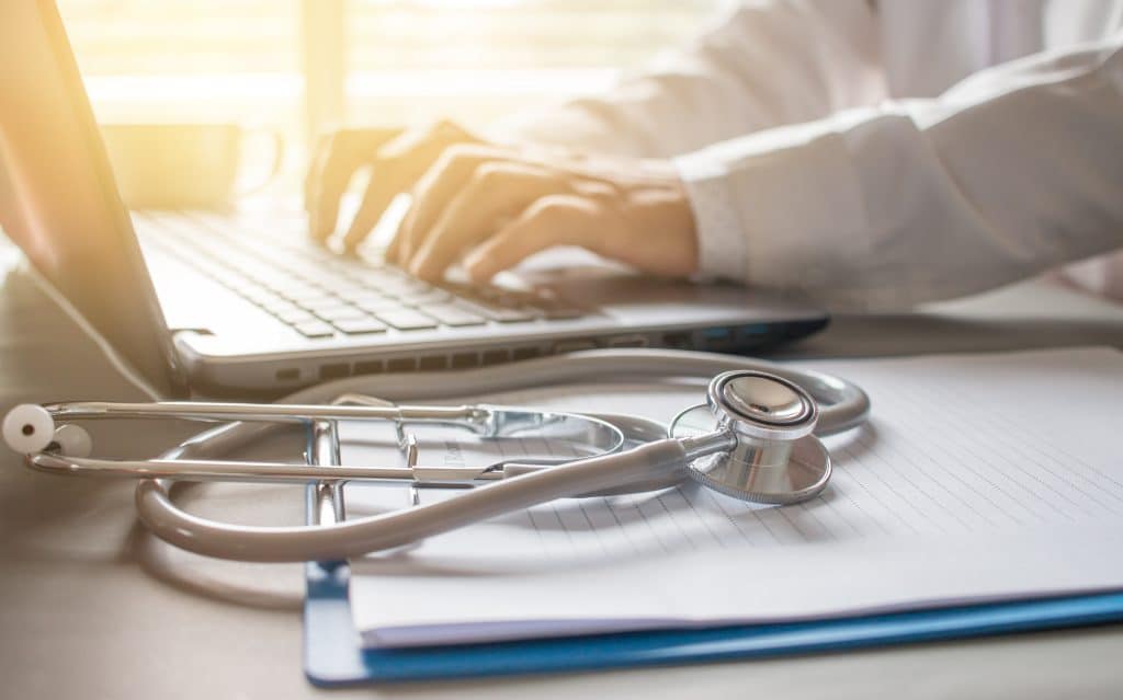 Stethoscope on prescription clipboard and Doctor working an Laptop